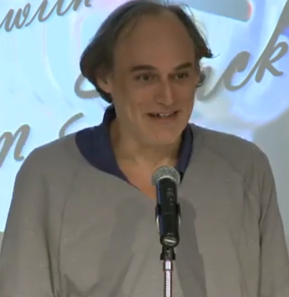Donald X. Vaccarino speaking at a microphone during a video appearance