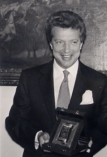 Black-and-white portrait photo of Vittorio Cecchi Gori holding an award plaque, wearing a suit and tie.