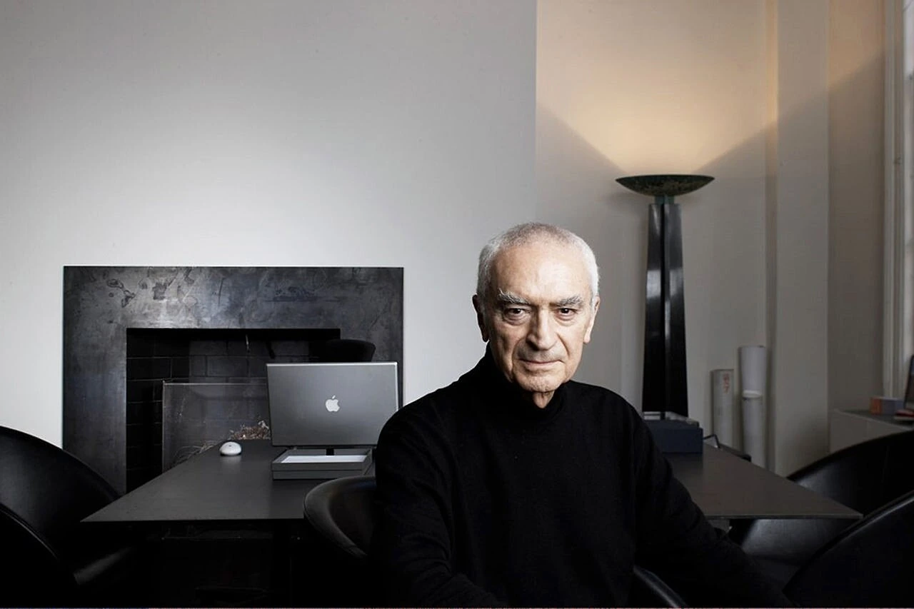 Massimo Vignelli seated in a modern interior, wearing a black turtleneck, photographed in a clean editorial style.