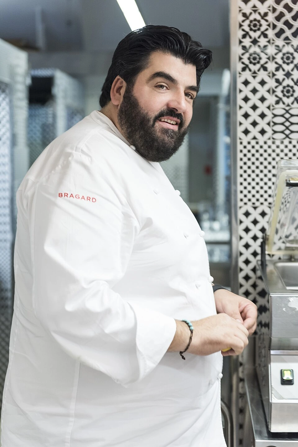 Antonino Cannavacciuolo in a kitchen wearing a white chef’s jacket, smiling toward the camera.
