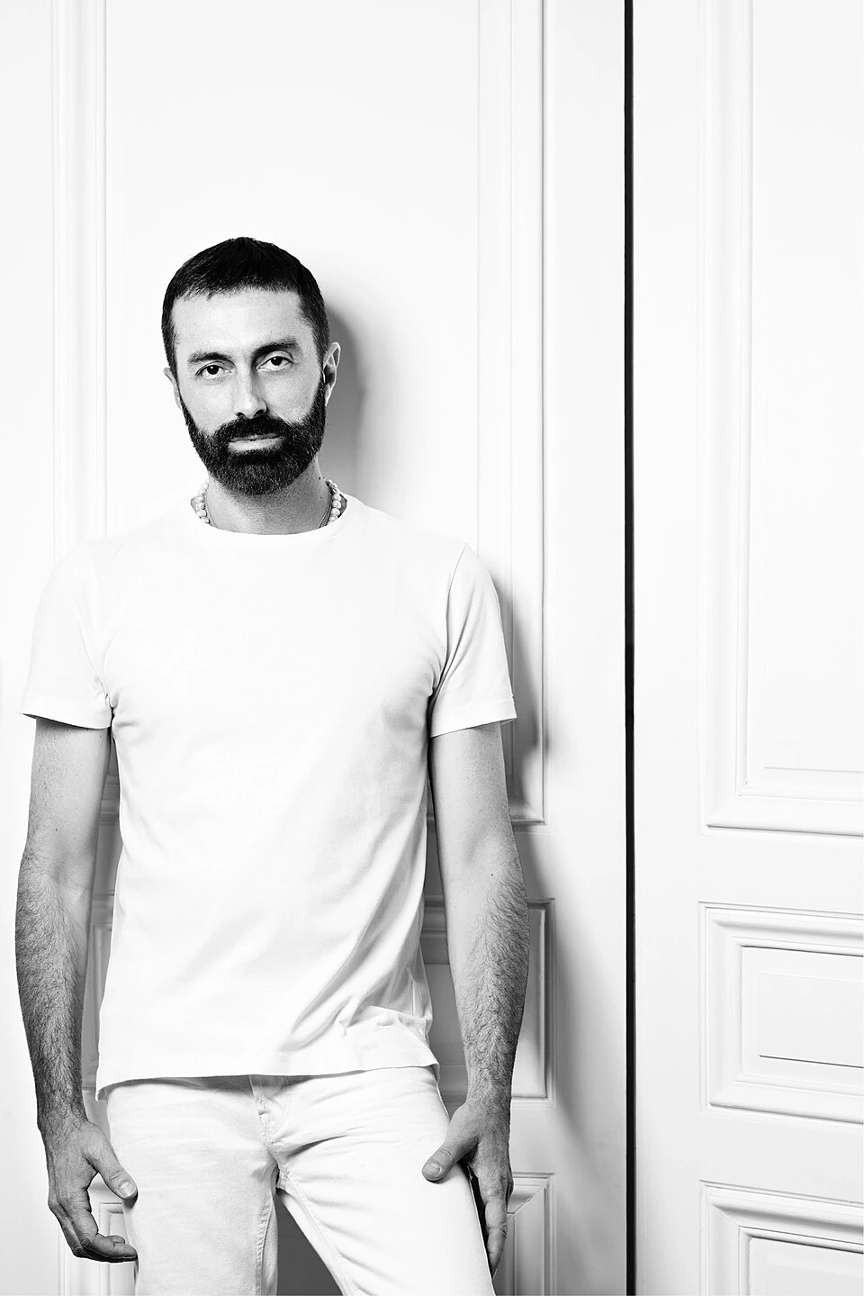 Portrait photo of fashion designer Giambattista Valli standing against a light background in a black-and-white editorial