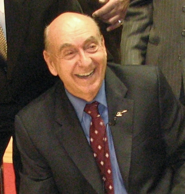 Dick Vitale smiling in a suit at a basketball event