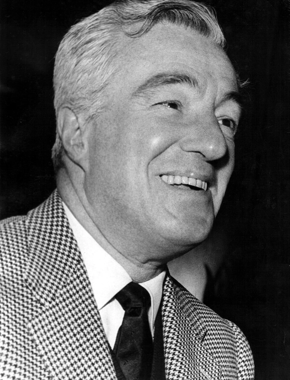 Black-and-white portrait of Vittorio De Sica smiling in a checkered jacket and tie.